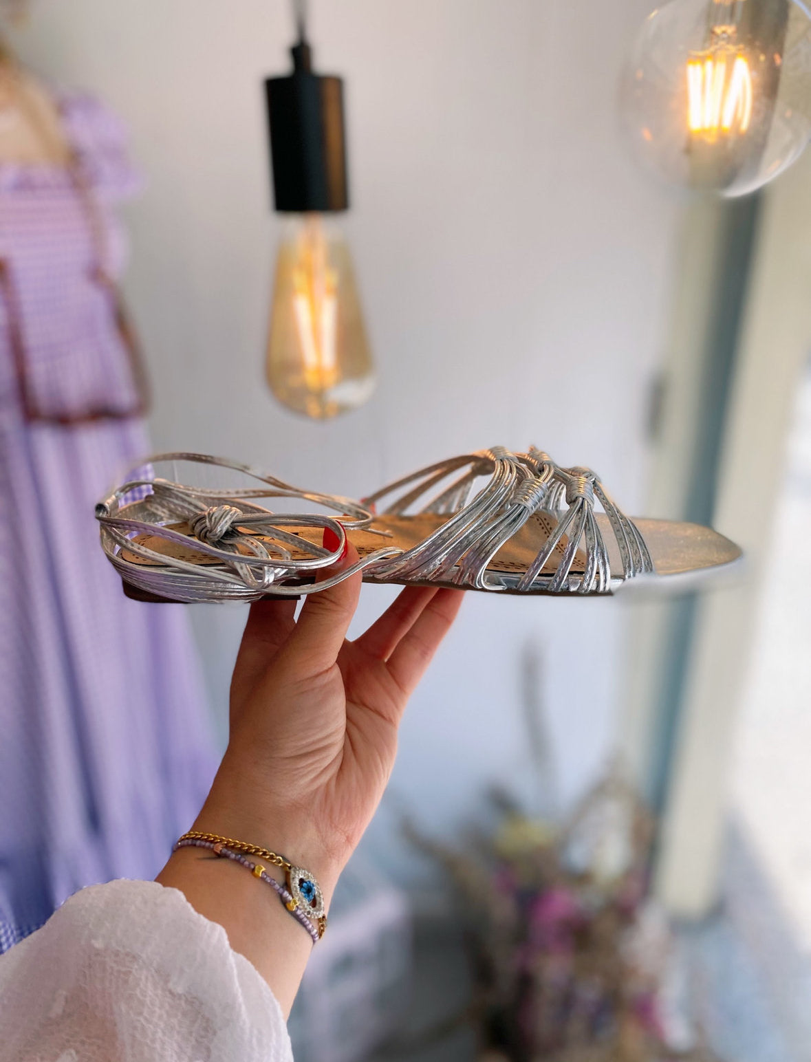 Sandalia plana con tiras de nudo plateadas y lazo en el tobillo.